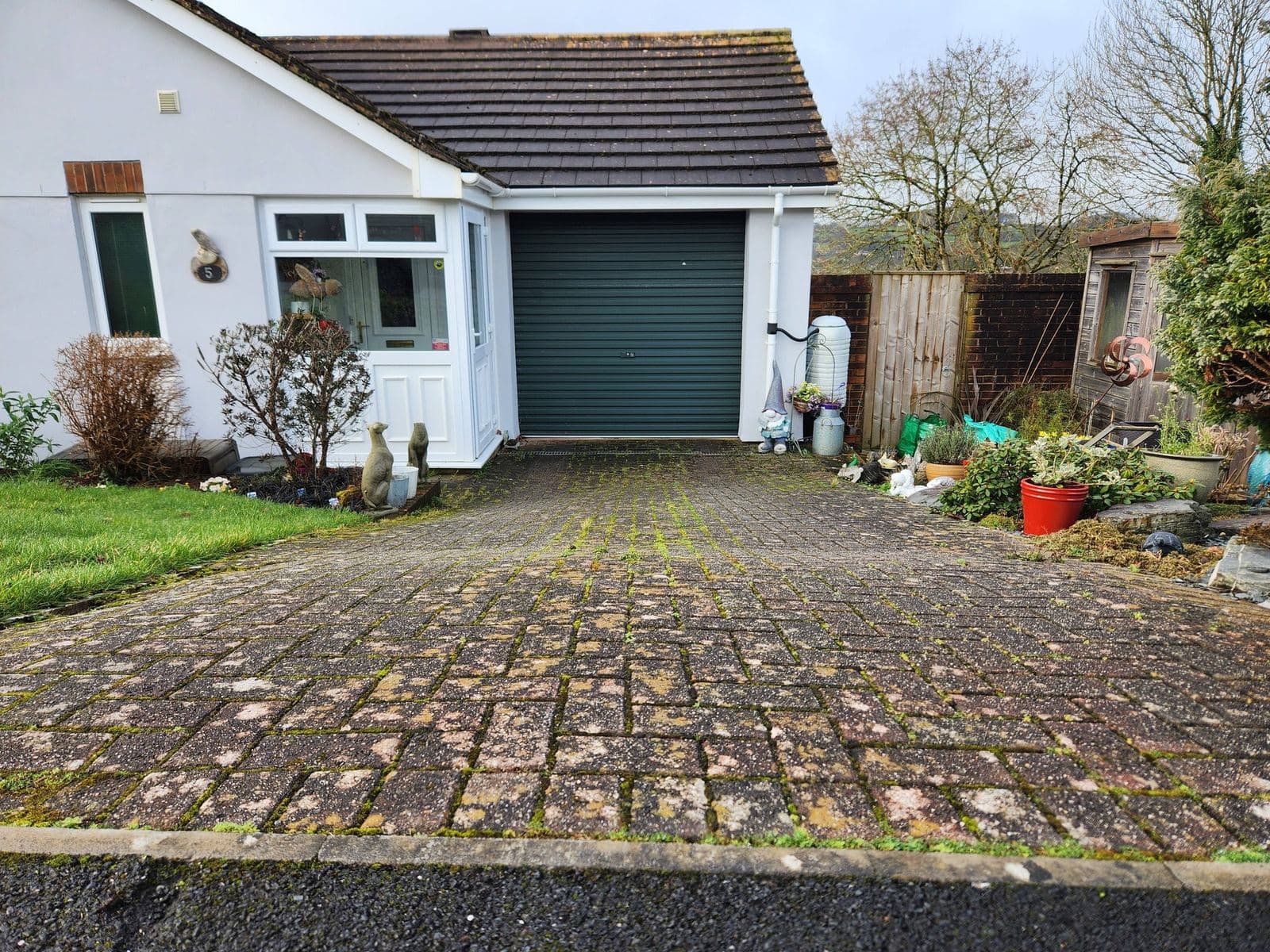 Driveway before — old mossy block paving with green garage door